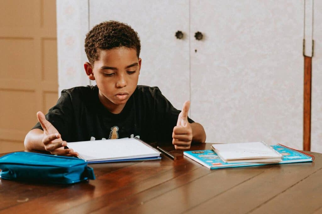 Young boy lifting hands as if confused by homework in front of him